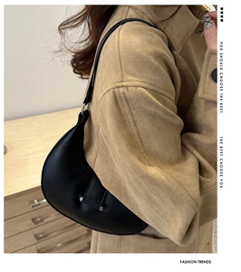 Side view of a black matte leather hobo bag worn with a khaki coat showing elegant crescent shape