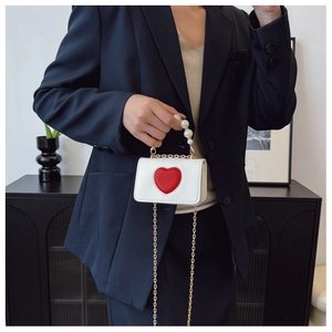 Detail of a white heart-shaped mini handbag with pearl handle and gold chain strap