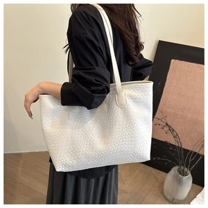 Detail view of white woven shoulder bag with fine texture and leather logo tag