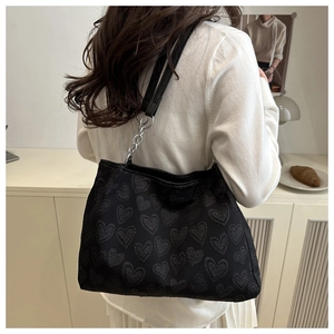 Detail of black heart-pattern tote bag featuring chain shoulder strap in lifestyle setting