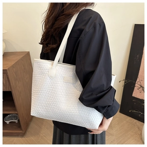 Close-up of a white woven tote bag featuring a leather brand tag and sleek shoulder strap
