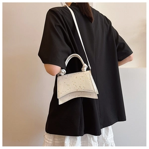 Détail du sac à main blanc à motifs étoiles avec base incurvée et poignée à nœuds stylée