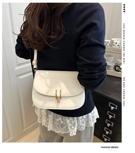 Detail of white matte leather saddle bag featuring a vertical gold buckle and thin strap
