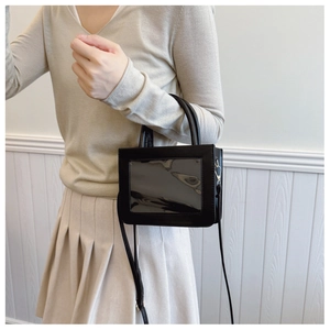 Detail of a chic black glossy square handbag featuring transparent panels and silver buckles