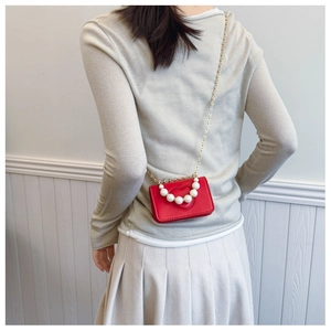 Detail of red heart-shaped mini bag with pearl handle and gold chain strap on model