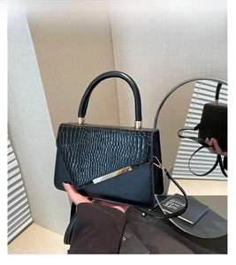Detail of black crossbody bag with faux crocodile flap and gold metal bar accent