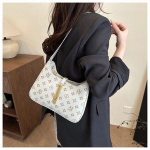 Detail of vintage white baguette bag with brown print and gold lock on shoulder