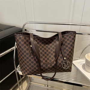 Dark brown tote bag with M-letter print and gold charm on a transparent shelf