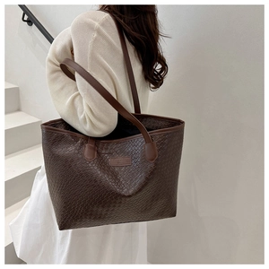 Detail of a large brown woven leather tote bag with shoulder straps worn by a model