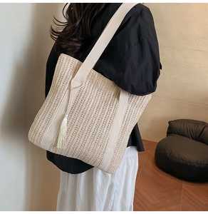 Dettaglio della borsa tote beige intrecciata a mano con nappa e tracolla larga