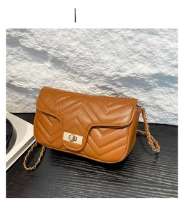 Détail d'un sac bandoulière matelassé marron avec fermoir tournant doré et bandoulière chaîne