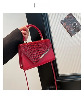 Detail of red croc-embossed leather handbag with gold metal trim and flap closure