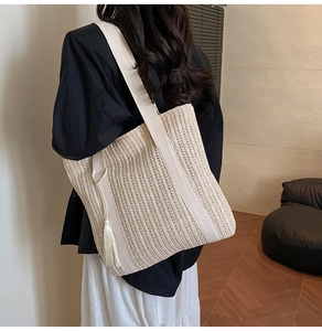 Dettaglio di una borsa tote in paglia intrecciata con nappa bianca e tracolla larga