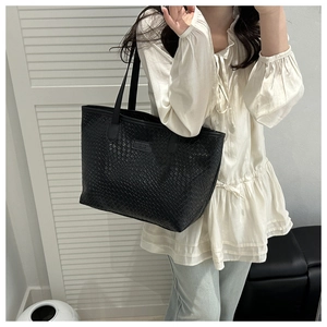 Detail of black woven texture tote bag with leather logo patch worn on shoulder