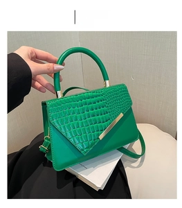 Detailed close-up of green crocodile texture handbag with gold metal bar on flap