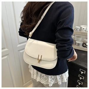Detail of cream saddle bag with golden rectangular metal lock and adjustable shoulder strap