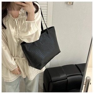 Detail of black woven leather tote bag showing fine square texture and shoulder strap