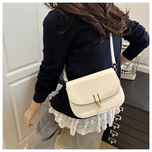 Close-up of minimalist beige leather crossbody bag with gold buckle on female model