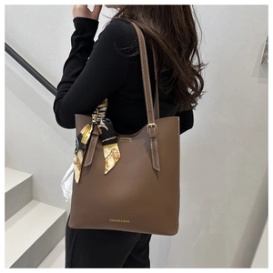 Detail of brown leather tote bag featuring golden logo and stylish patterned silk scarf