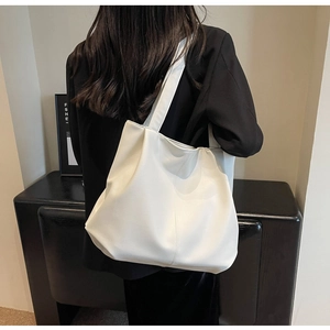 Gros plan d'un sac cabas blanc en similicuir texturé porté à l'épaule par un mannequin
