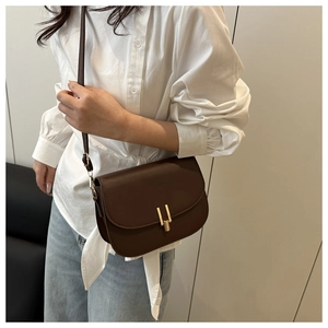 Brown leather crossbody bag with gold clasp shown on model wearing white shirt and jeans