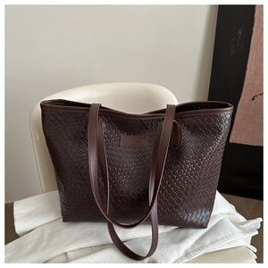 Detailed view of dark brown woven faux leather tote bag with brand logo patch and straps