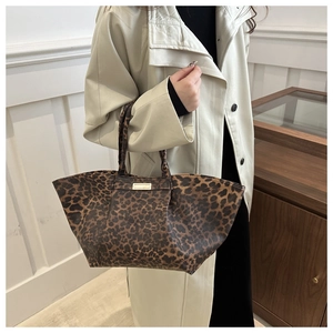 Detail of leopard print tote bag with gold metal plate held by model in trench coat