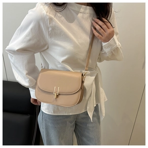 Detail of beige leather saddle bag with gold metal clasp and adjustable shoulder strap