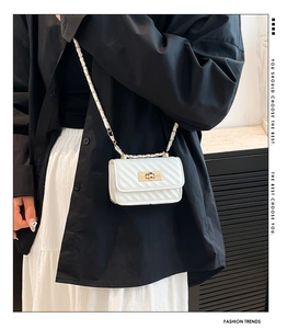 Detail of white quilted mini chain bag with gold lock worn by model in fashion setting