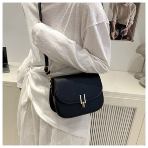 Detail of a black semi-circle saddle crossbody bag with minimalist gold metal hardware clasp