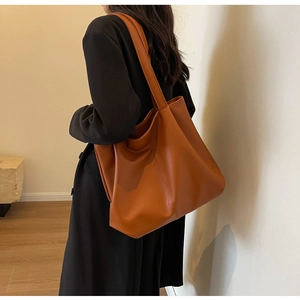 Vue latérale d'un grand sac cabas marron en cuir porté par un mannequin en studio épuré