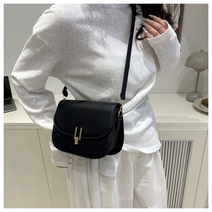 Detail of minimalist black leather crossbody bag featuring a golden U-shaped clasp closure