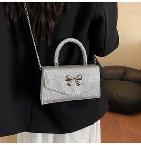 Mini sac argenté pailleté avec nœud en métal et bandoulière porté par un mannequin
