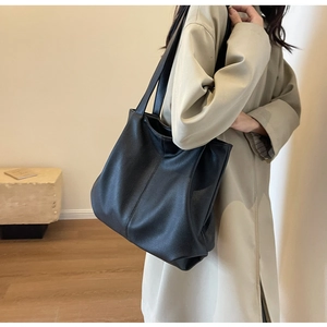 Gros plan du grand sac cabas noir à texture grainée porté à l'épaule par le mannequin