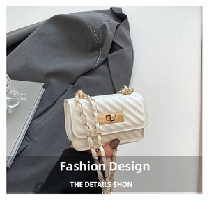 Close-up of white quilted crossbody bag with gold lock and chain strap on grey blazer