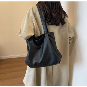 Gros plan du sac cabas en cuir grainé noir porté avec un trench-coat classique beige