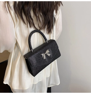 Détail d'un sac noir pailleté avec boucle papillon argentée porté par un mannequin