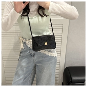 Detail shot of woven leather texture on black crossbody bag with gold metal square buckle