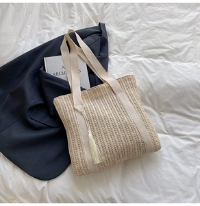 Dettaglio di una borsa tote intrecciata beige con nappa a frange su letto bianco
