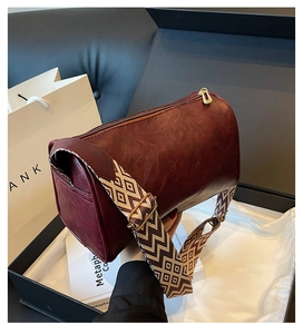 Detail der burgunderroten Zylindertasche mit edler Textur und gemustertem Gurtband