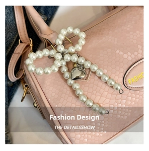 Detail of a pearl bow charm with silver heart pendant on a pink embossed handbag