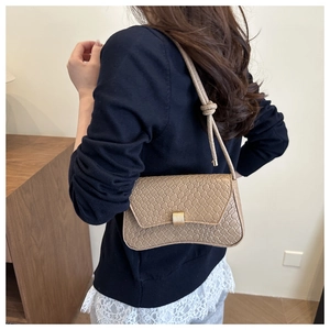 Detail of beige woven baguette bag featuring a gold square buckle and knotted strap detail