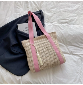 Dettaglio borsa shopper in paglia intrecciata con manici rosa e nappa su fondo bianco