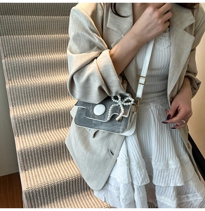 Détail du sac bandoulière gris et blanc avec pendentif en perles et fermoir rond chic