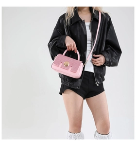 Detail of pink leather crossbody bag with gold round buckle and textured flap shown on model