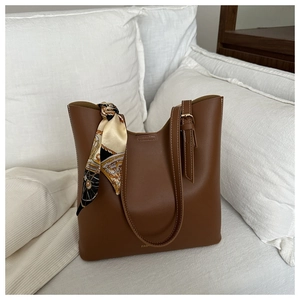 Detail of caramel brown leather tote bag with vintage printed silk scarf on white sofa