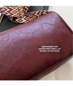 Nahaufnahme der weinroten Lederbeuteltasche mit einem geometrisch gewebten Schultergurt