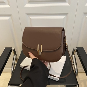 Minimalist dark brown leather crossbody bag with elegant gold metal latch on a chair