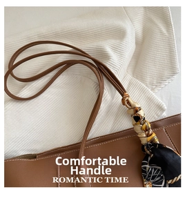 Detail of brown leather tote bag featuring white stitching and silk scarf on handle