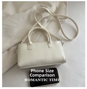 Detailed view of cream white shoulder bag with embossed letters next to a smartphone